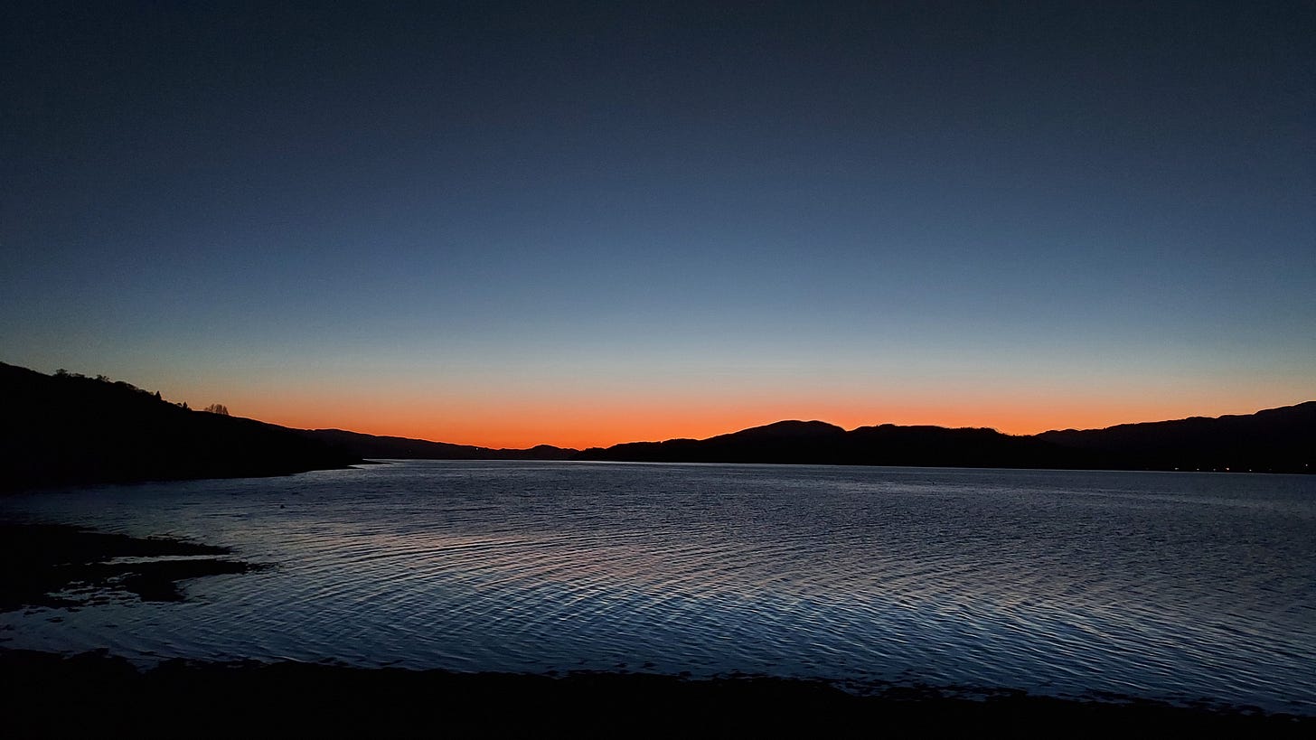 Winter sunset over a Scottish loch with a clear sky with a band of orange fading up to deep blue, and hills on the horizon
