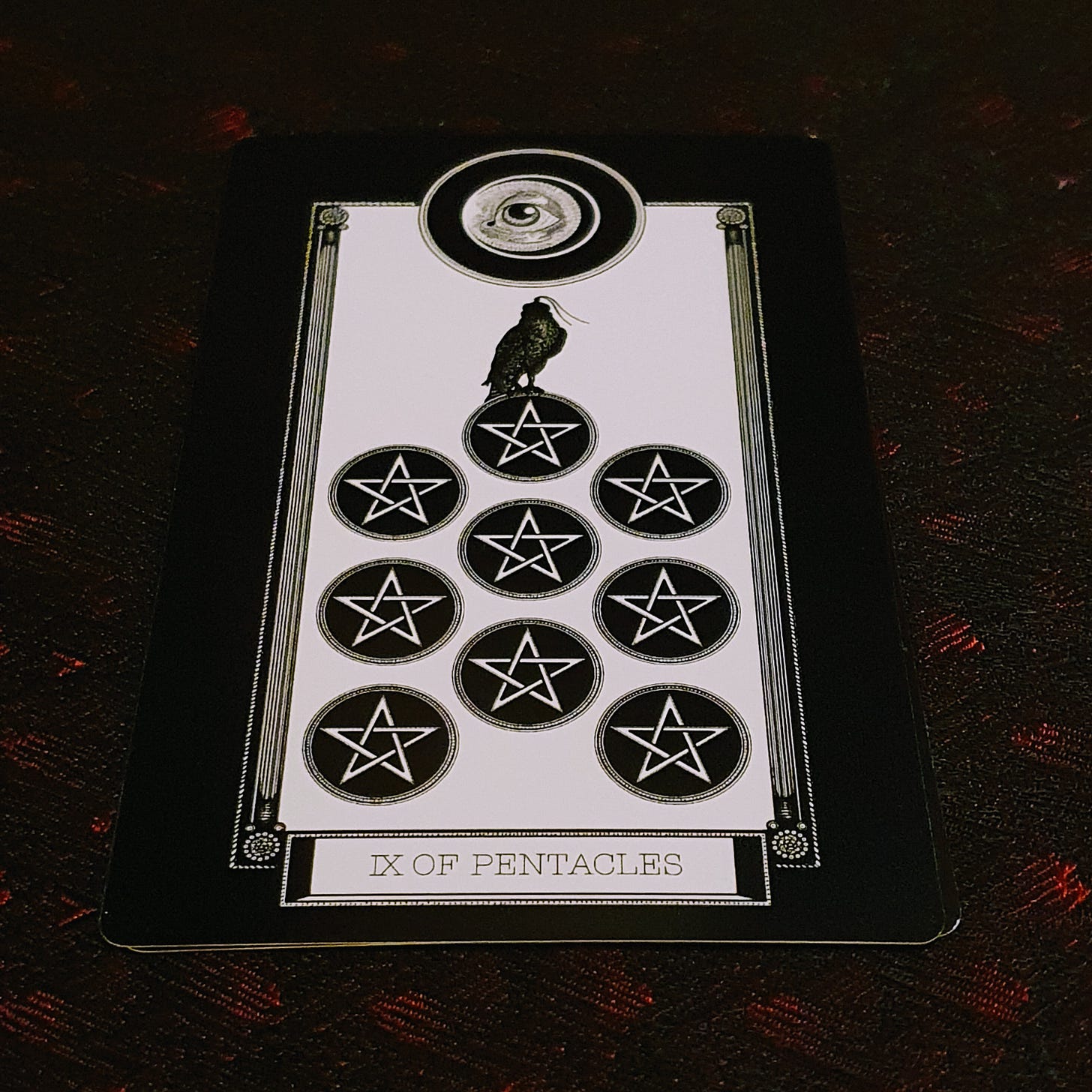 The Nine of Pentacles card sits on black and red silk The Nine of Pentacles card sits on black and red silk