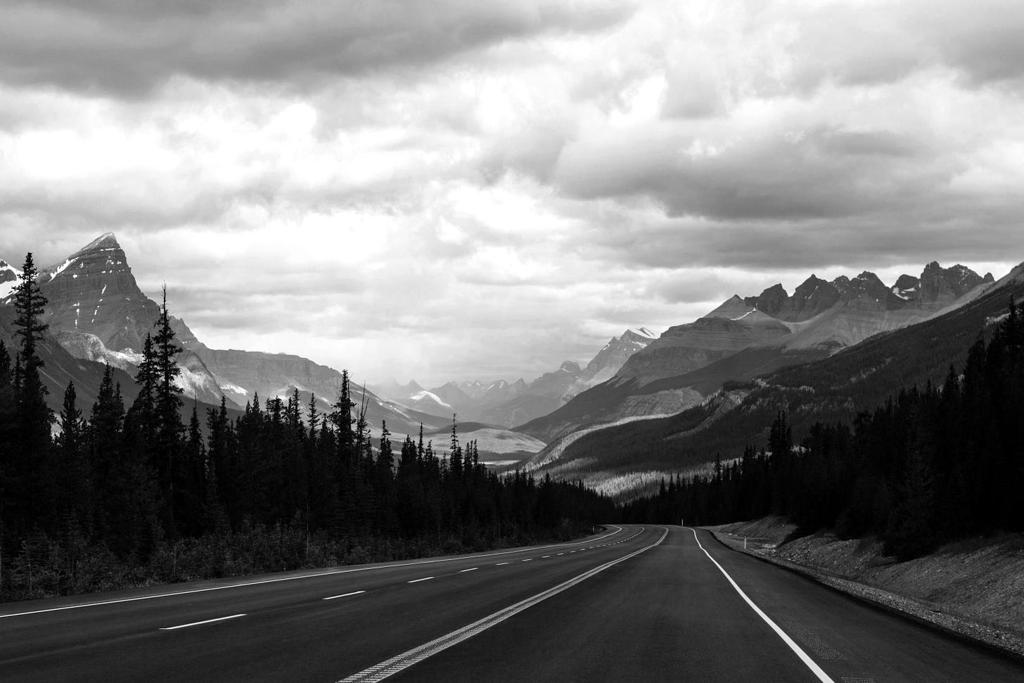 gray concrete road near green trees and mountains during daytime