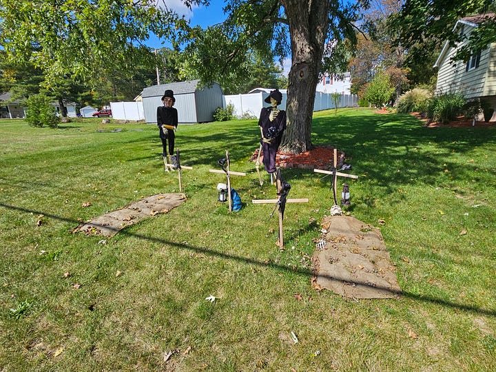 Halloween decorations, including skeletons sitting outside a tent, a skeleton in a coffin, and skeletons attending a funeral.