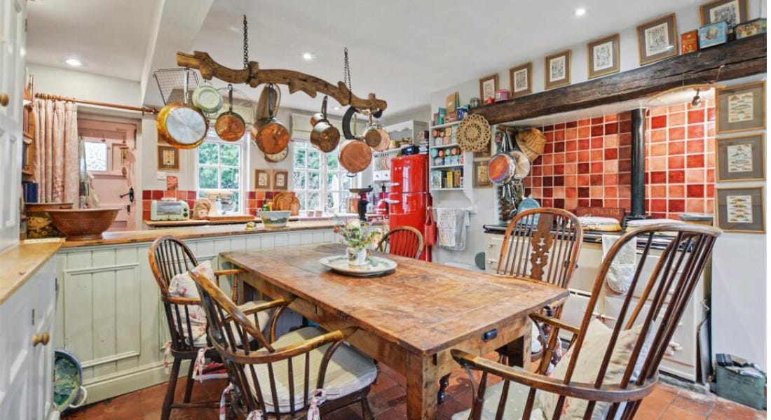 A kitchen with a wooden dining table, copper pots and pans on the ceiling, a red oven, and mint green paneling