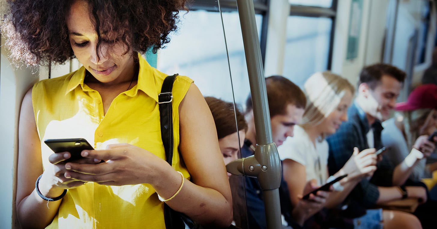 Standing commuter in yellow shirt on their phone, with other seated commuters also on their phones in the background