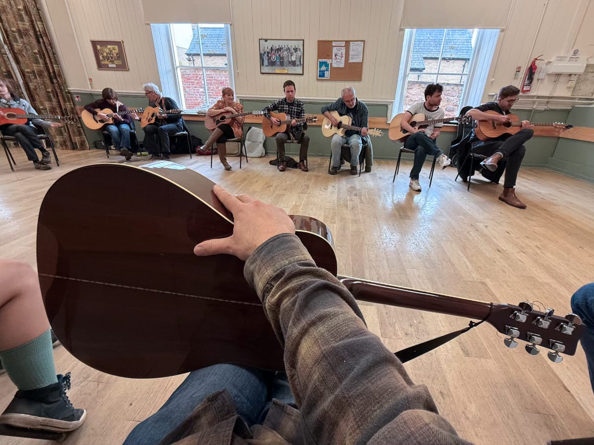 A circle of chairs all with people sat with guitars on them A circle of chairs all with people sat with guitars on them
