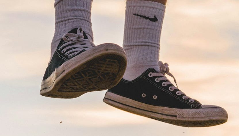 person wearing black low-top sneakers jumping high under white sky