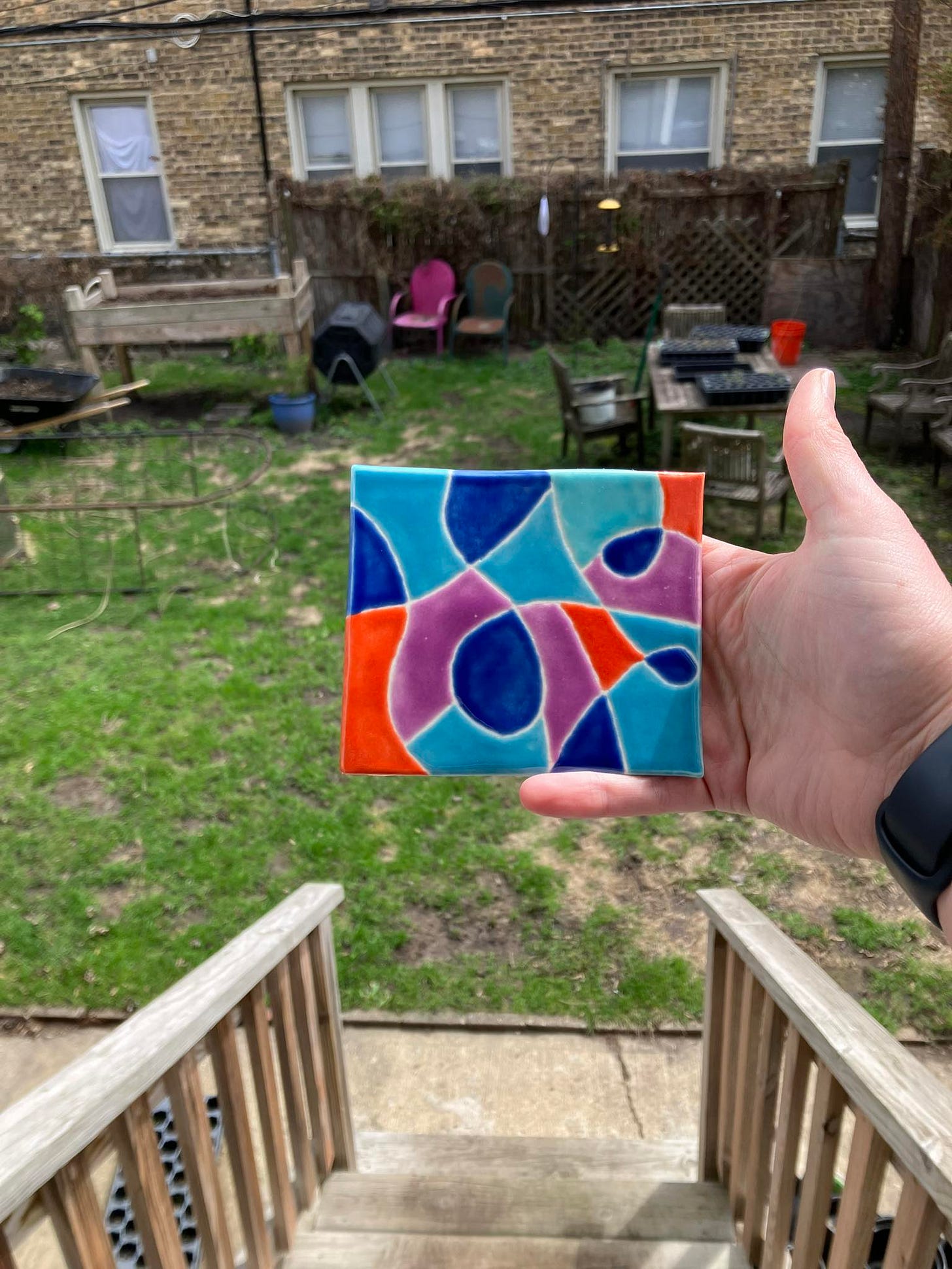 test tile with blues, teal, purple, orange-red and drawn in loops in front of a brick apartment building