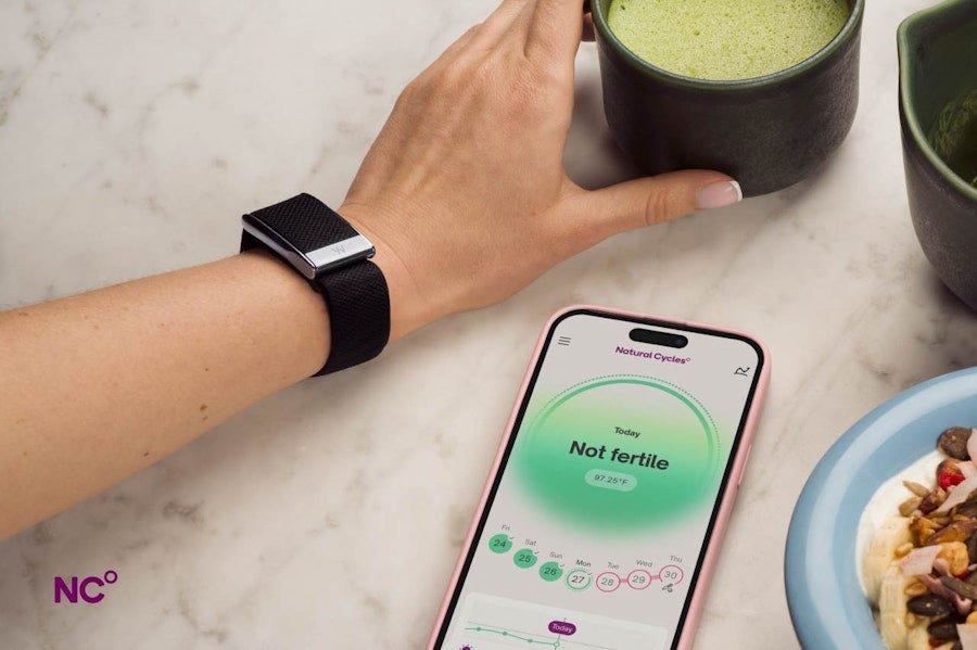 Arm wearing WHOOP reaching for macha, phone on the table next to breakfast showing Natural Cycles app