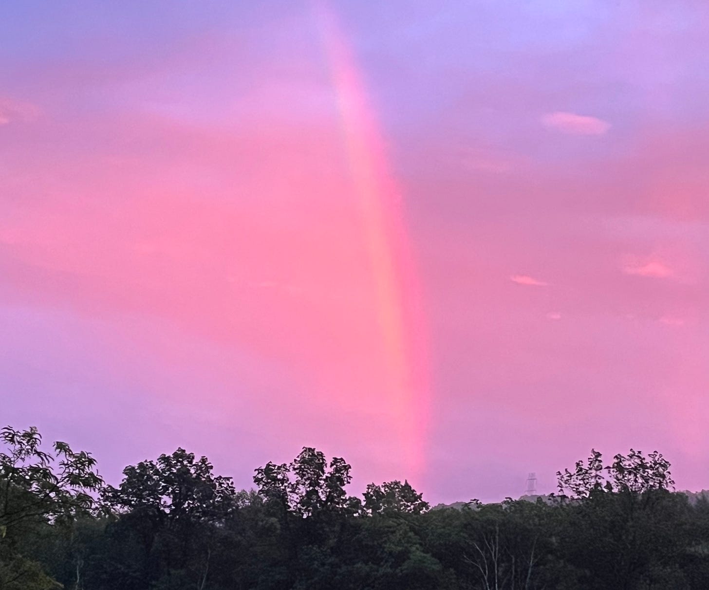 Photo of a pink and purple sunset sky with a vertical streak that's supposed to be a rainbow, but doesn't really look like one in this photo.