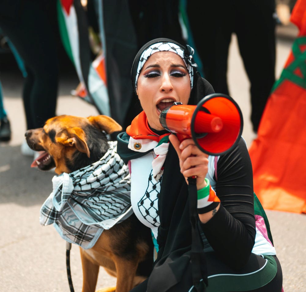 Pro-Palestinian Arab woman shouting on bullhorn while wearing Pro-Hamas garb, holding dog wearing kaffiyah