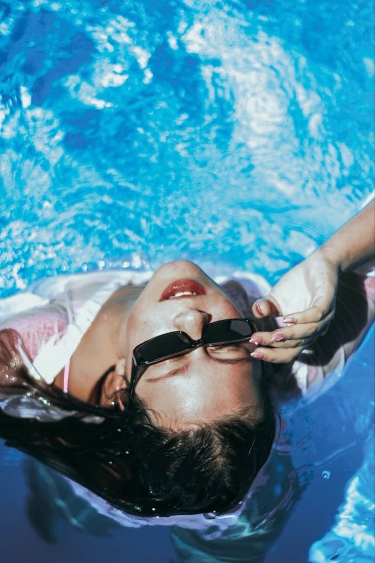 This may contain: a woman wearing sunglasses floating in a pool with her head above the water's surface