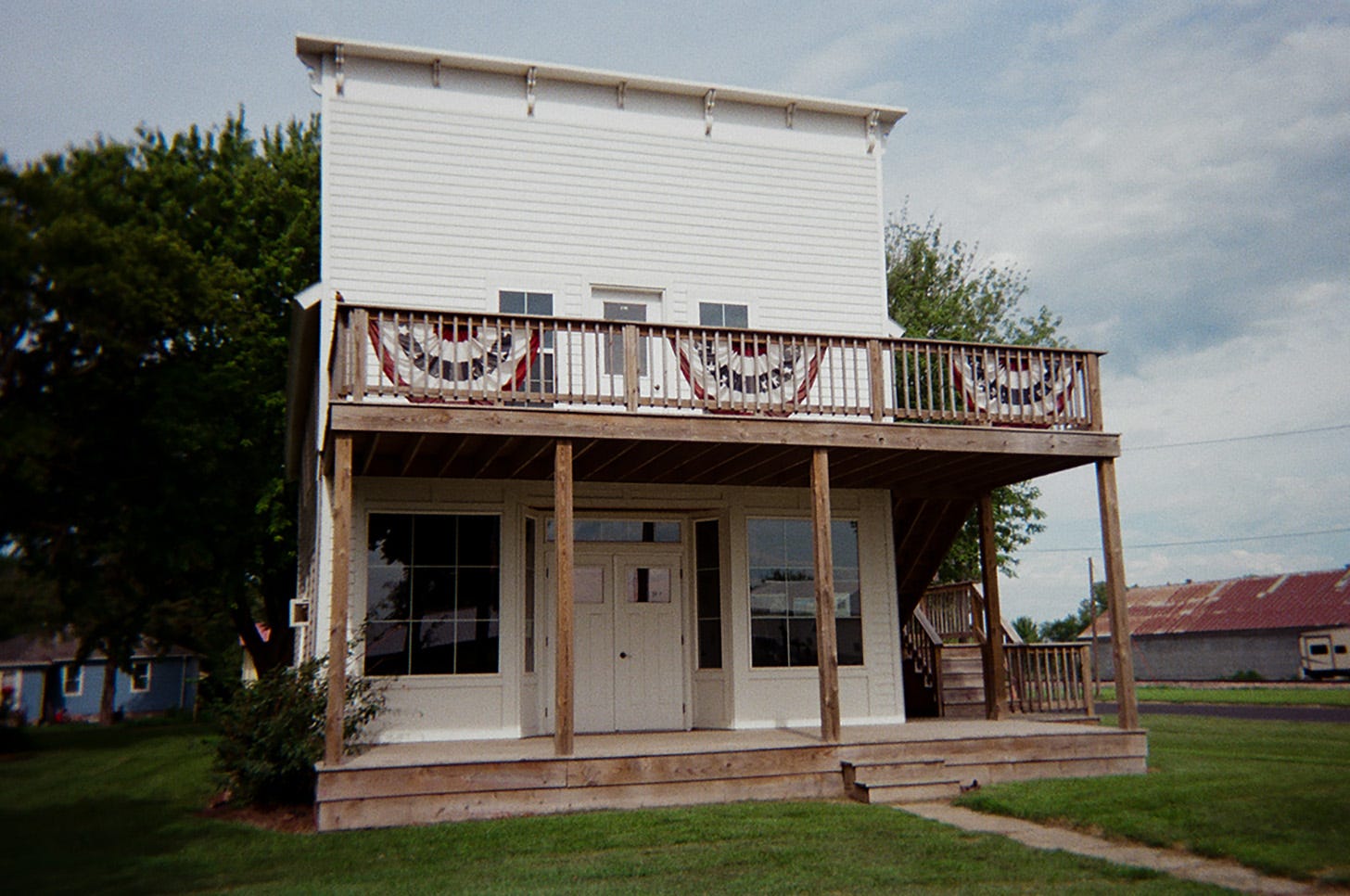 A small, white, two-story store with wooden porch and deck.
