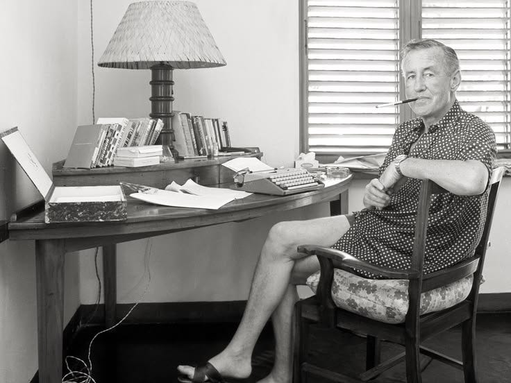 This may contain: an old man sitting in a chair at a desk with a lamp and books on it