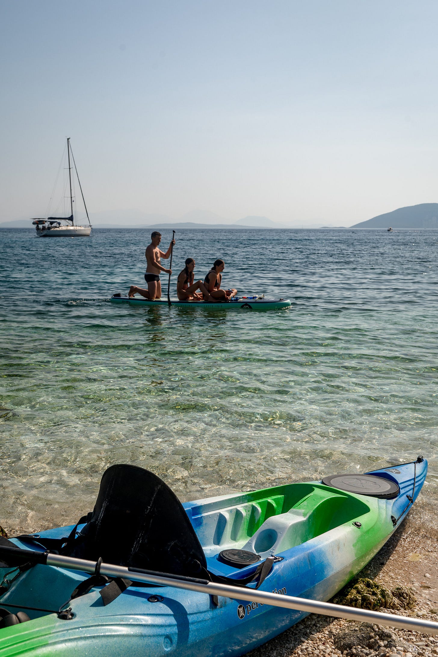 Three people sit in a kayak in the shallows on a picturesque beach.