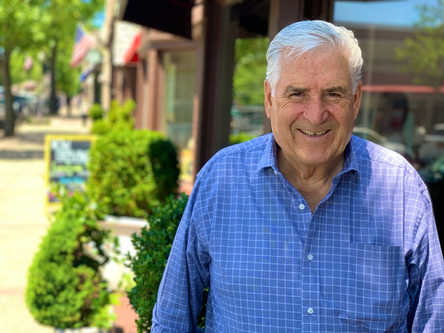 White man, blue shirt, smiling, outdoors of a sunny street