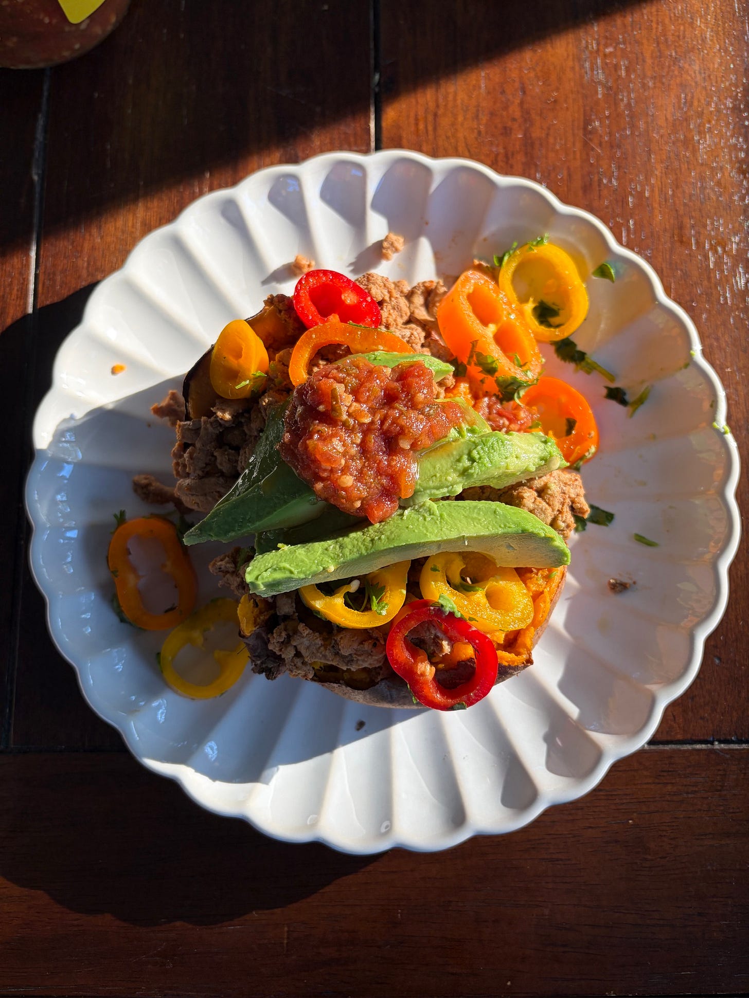 A stuffed sweet potato taco bowl topped with seasoned ground turkey, colorful sliced bell peppers, fresh avocado, chopped cilantro, and a spoonful of red salsa, served on a white plate with a lime wedge on the side