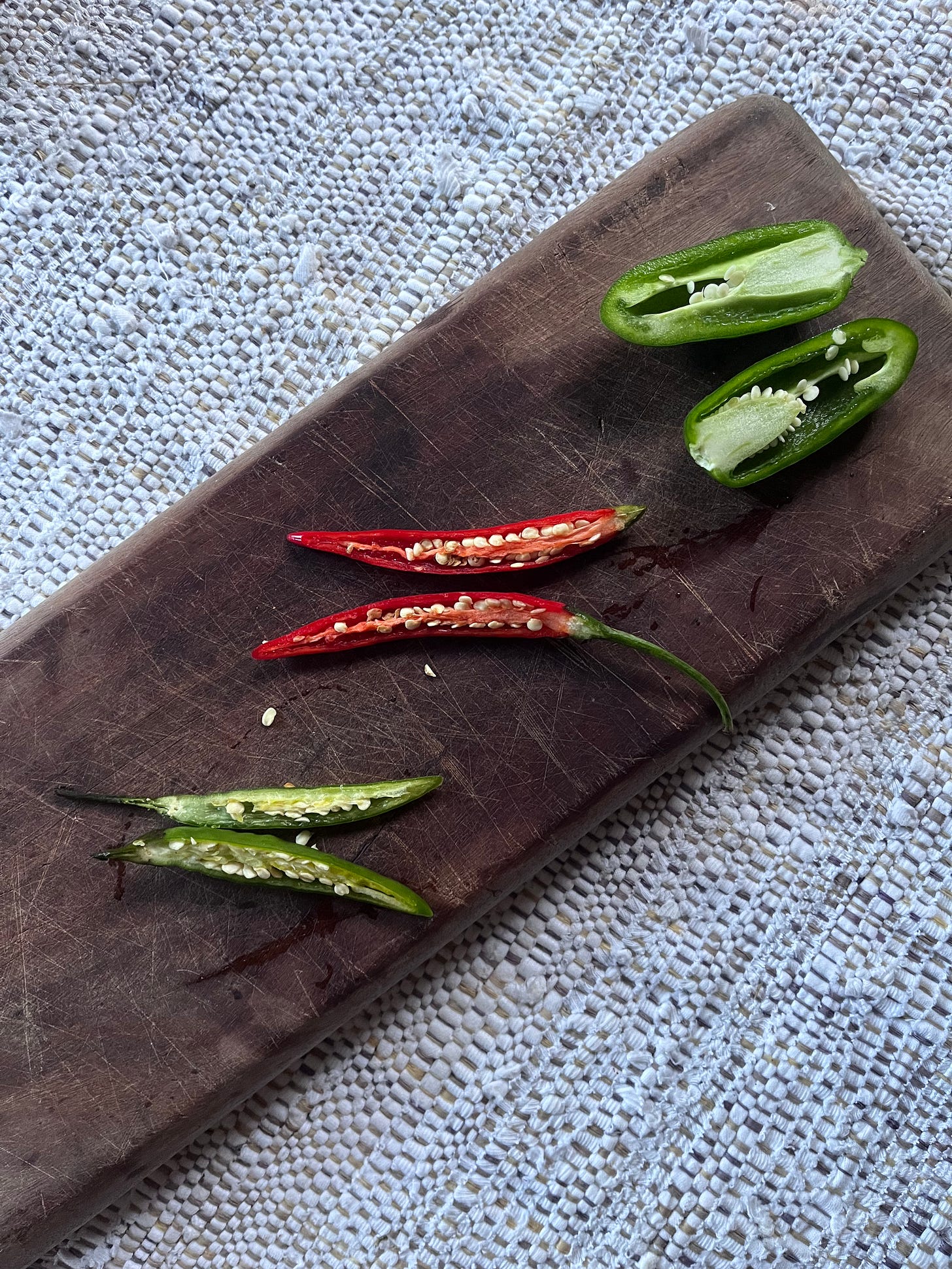 three chillies lined up on a wooden board, all cut lengthways to show their placentas.