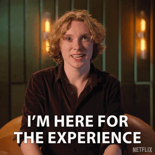 a man is sitting in front of a sign that says i 'm here for the experience by netflix a man is sitting in front of a sign that says i 'm here for the experience by netflix