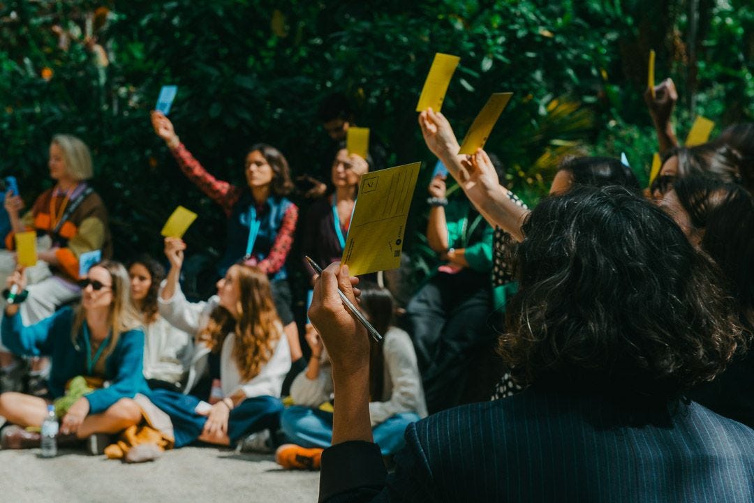 An image taken at the May 2025 Future Days festival. The image shows a group of people holding up blue and yellow voting ballots. An image taken at the May 2025 Future Days festival. The image shows a group of people holding up blue and yellow voting ballots.
