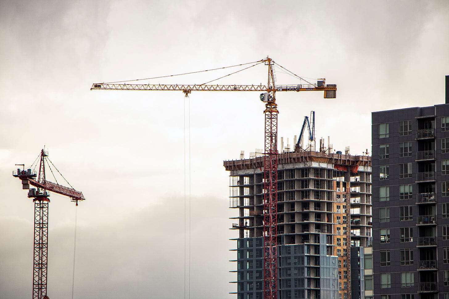 two cranes are seen around an unfinished tower of condos on a clowdy day