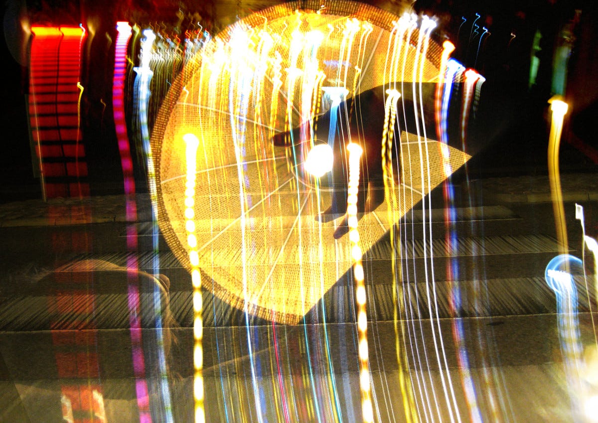 Collage consisting of photographs taken by my seventeen-year-old self: a human figure reaching a hand up to the shining light bulb of a lamp, with an overlay of lights in colors of yellow, red, blue and orange, on the background of an image of a pedestrian crossing