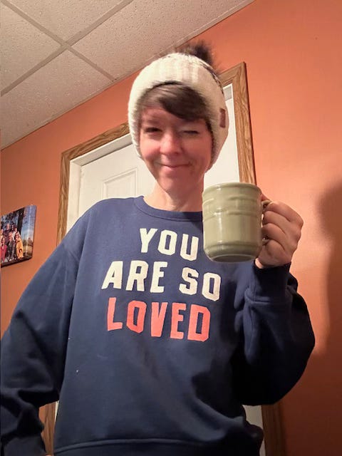 A women with a white beanie cap and navy sweatshirt is holding a green mug and winking. A women with a white beanie cap and navy sweatshirt is holding a green mug and winking.