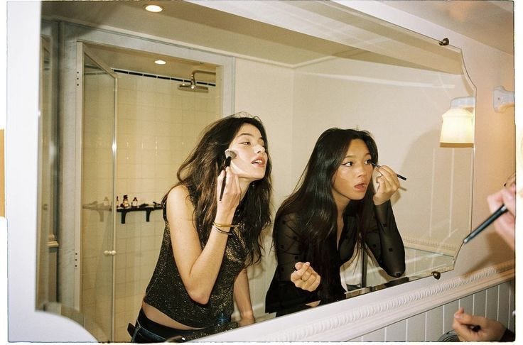 This may contain: two women are brushing their teeth in front of the mirror and one is looking at her reflection This may contain: two women are brushing their teeth in front of the mirror and one is looking at her reflection