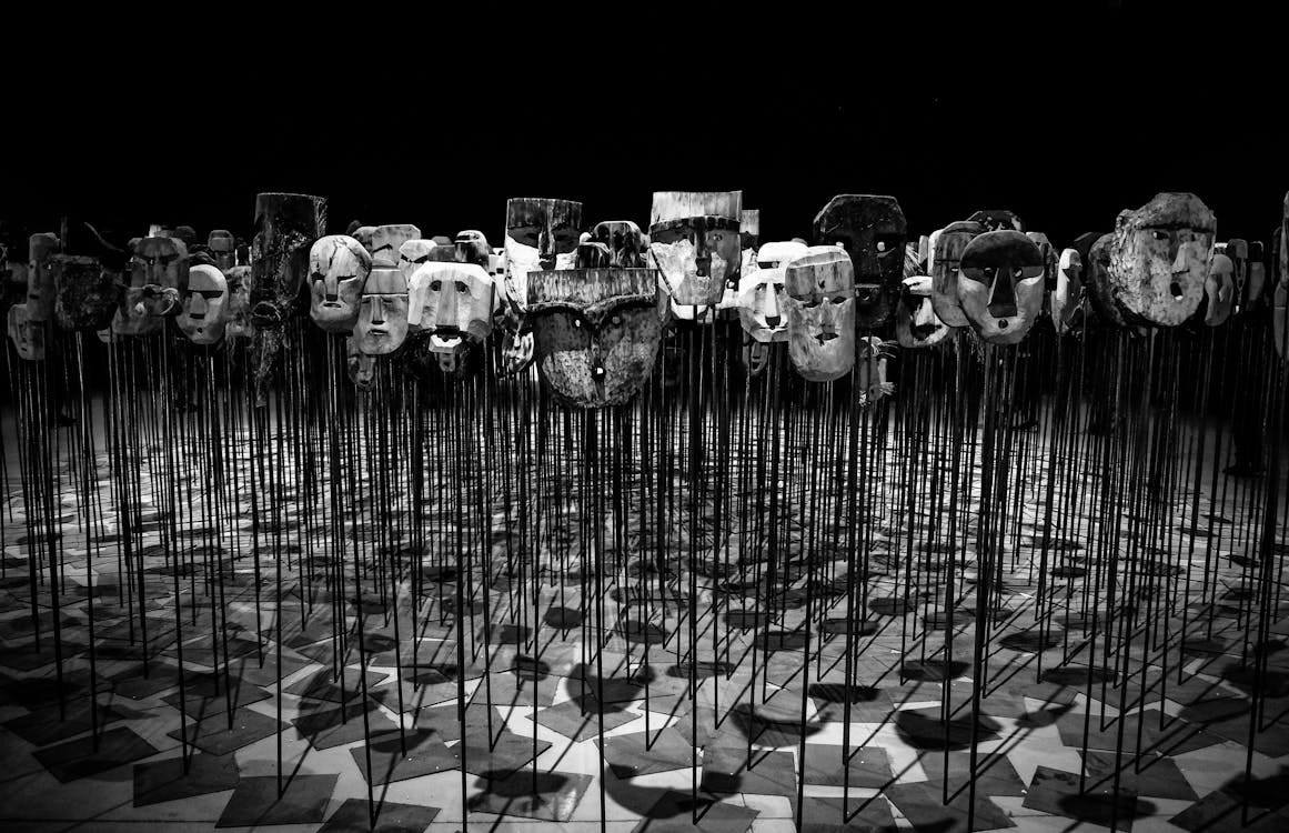 Free An artistic display of wooden masks on poles, set in a dimly lit theater. Stock Photo