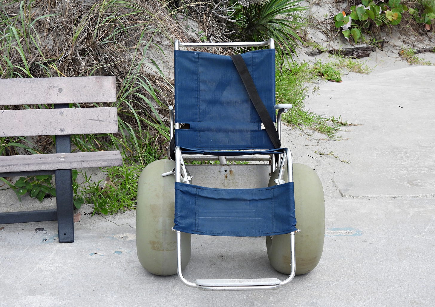 Blue beach wheelchair with tan inflatable wheels next to a bench on a beach