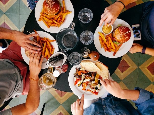 Hands of three people touching plates of hamburgers and fries on a round, black table.