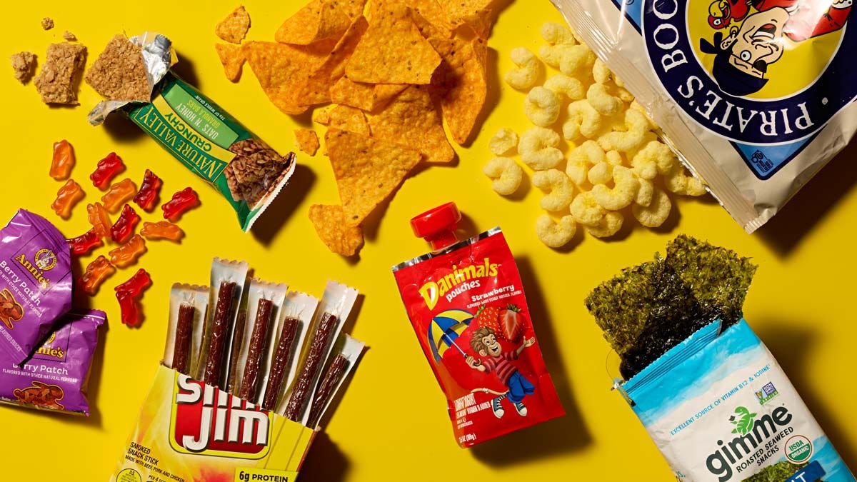 Annie's Organic Fruit Snacks Berry Patch, Pirate's Booty Aged White Cheddar Puffs, Doritos Nacho Cheese Tortilla Chips, Slim Jim Mild Snack Size Sticks, Gimme Roasted Seaweed Snacks Sea Salt, Nature Valley Crunchy Granola Bars Oats 'n Honey, and Dannon Danimals Yogurt Pouch Strawberry arranged on a bright yellow background Annie's Organic Fruit Snacks Berry Patch, Pirate's Booty Aged White Cheddar Puffs, Doritos Nacho Cheese Tortilla Chips, Slim Jim Mild Snack Size Sticks, Gimme Roasted Seaweed Snacks Sea Salt, Nature Valley Crunchy Granola Bars Oats 'n Honey, and Dannon Danimals Yogurt Pouch Strawberry arranged on a bright yellow background