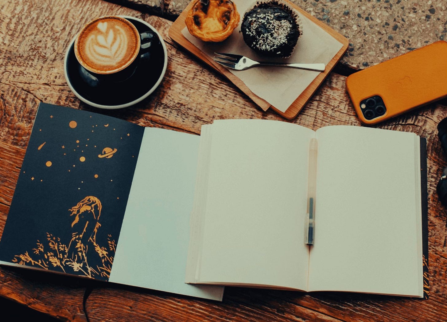 Table with coffee, a muffin, a notebook and a pen