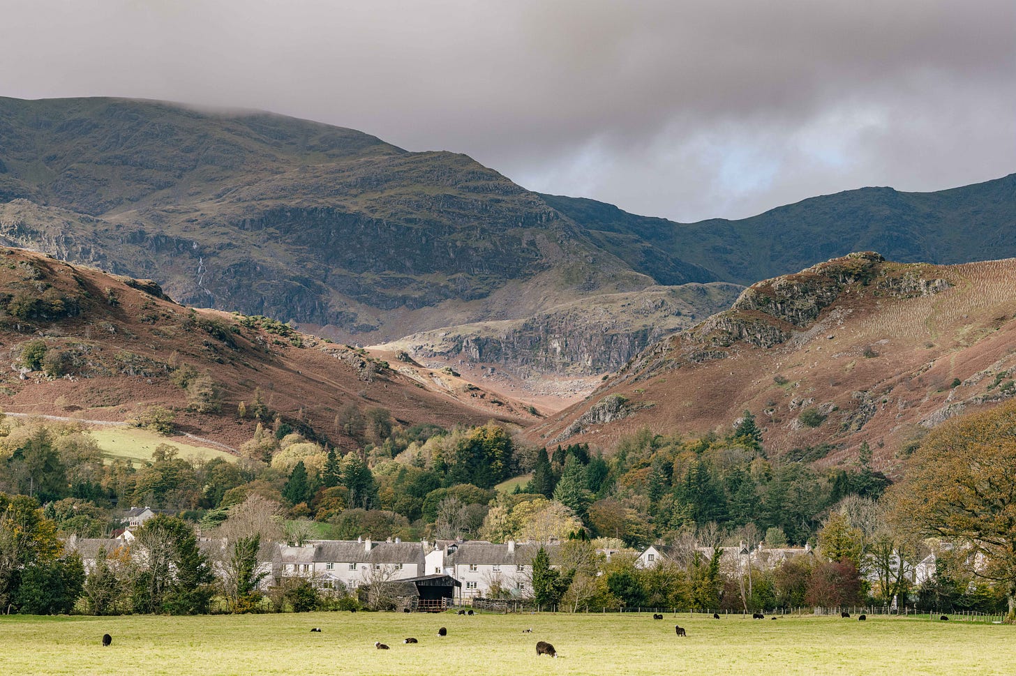 Wide view of mountains and village at the base of a valley in the Lake District, Cumbria, UK, autumn colours and grazing sheep. Wide view of mountains and village at the base of a valley in the Lake District, Cumbria, UK, autumn colours and grazing sheep.