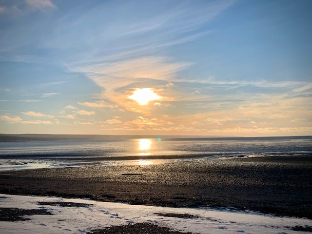 a sun sits low to the horizon over a rocky beach