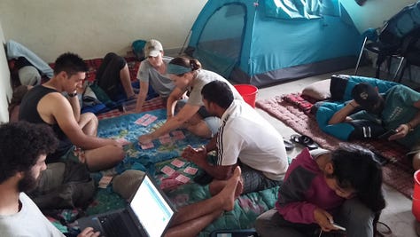 Pictures of life volunteering in disaster relief in Nepal. Tents in a courtyard, people sitting around reading books and playing games, standing on top of a damaged building, and buckets they used for washing.