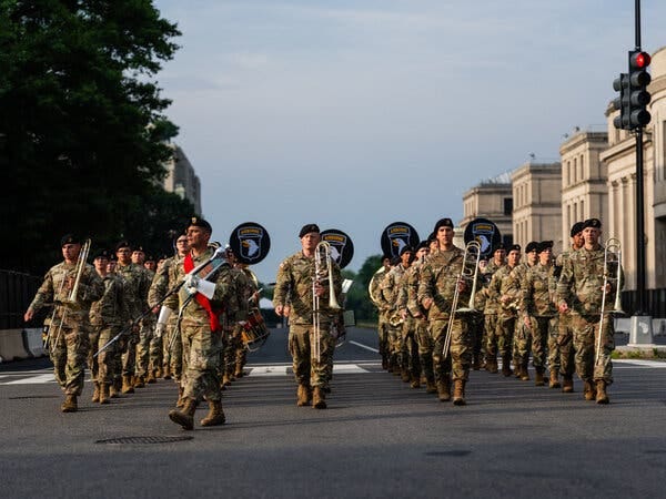 Soldiers in fatigues marching down a street in columns with musical instruments.