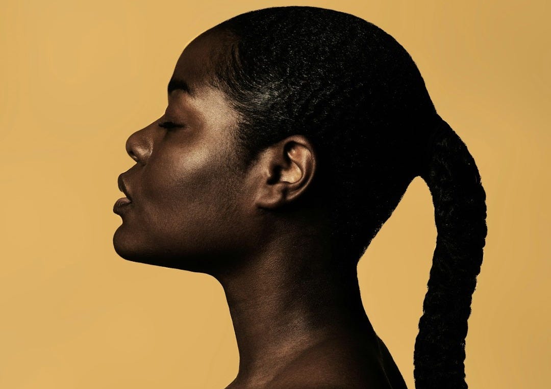braided woman taking photo beside yellow painted wall
