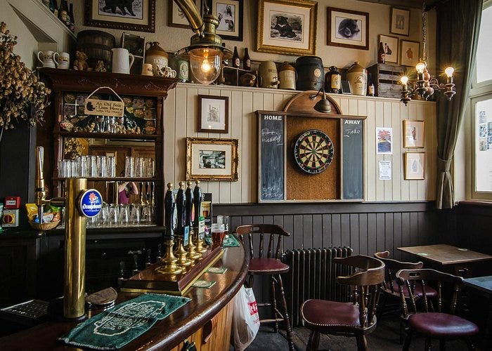 The curved bar of the Bear Inn, hop bines visible above it, a bank of four handpumps and a brass keg font top the bar