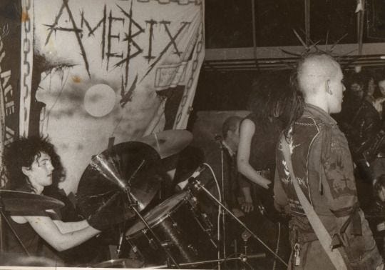 This may contain: an old black and white photo of some people playing instruments in front of a wall with graffiti on it