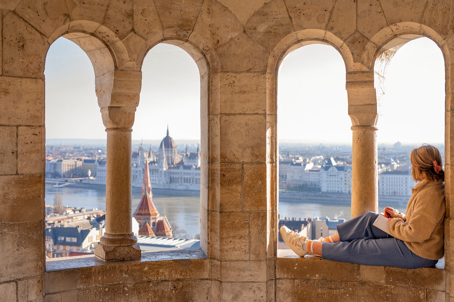 Woman sitting in a stone archway overlooking the Danube River and the Hungarian Parliament Building in Budapest. Woman sitting in a stone archway overlooking the Danube River and the Hungarian Parliament Building in Budapest.