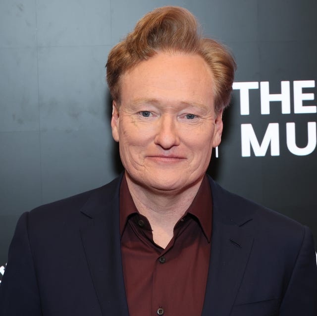 conan obrien smiles at the camera, he wears a navy suit jacket and red collared shirt conan obrien smiles at the camera, he wears a navy suit jacket and red collared shirt