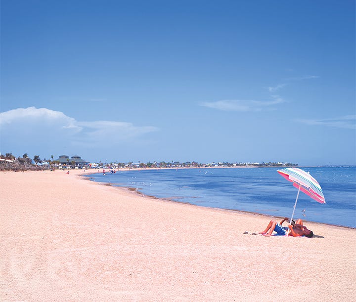 Left: photo of Rockport beach park, isolated with just a single beach umbrella and a person laying underneath, and a sunny sky. Right: a sunset shot taken at Ingleside, Texas, showing a calm water reflection of a pelican sitting on a pier.