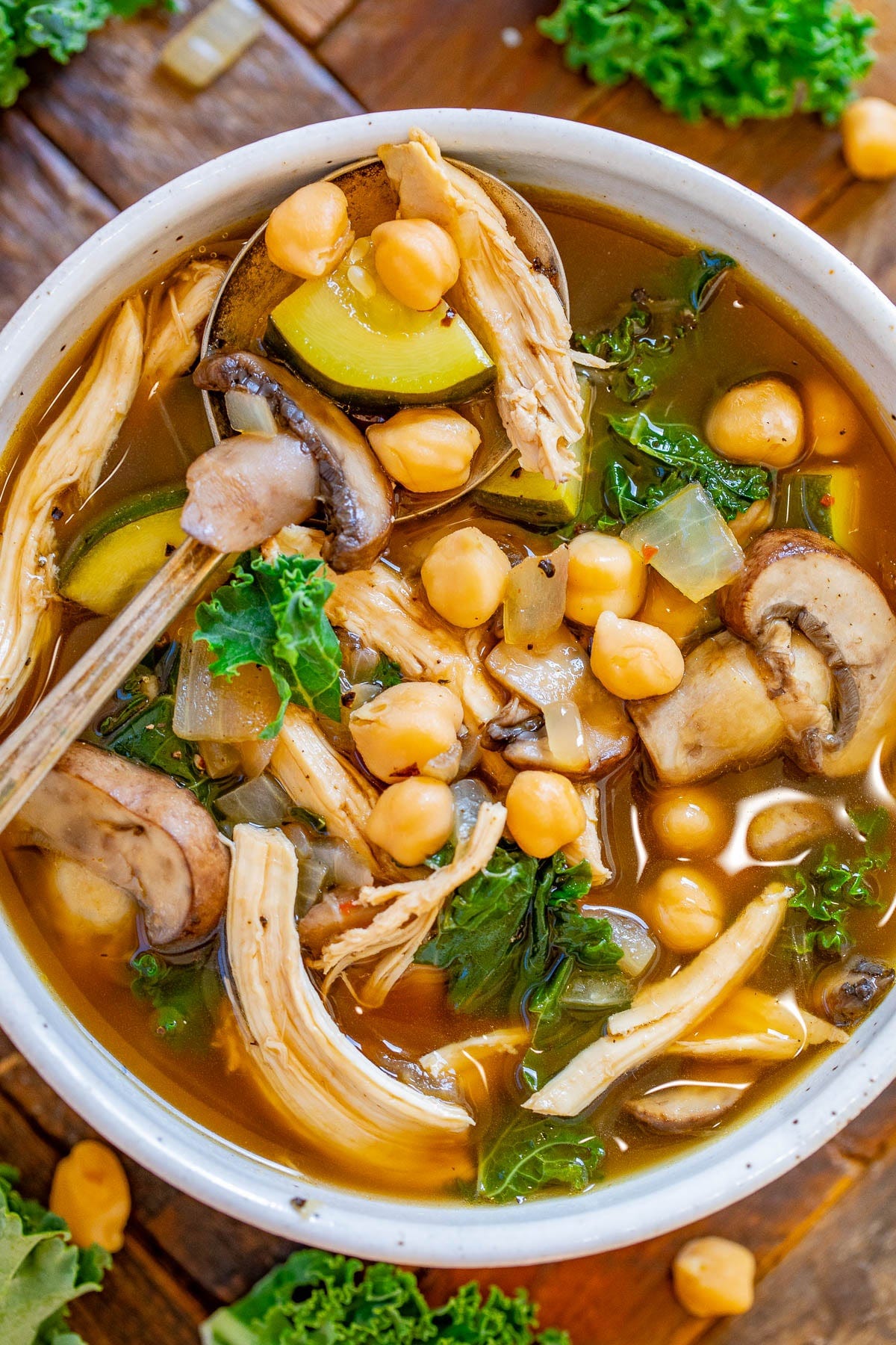 A bowl of chicken and chickpea soup with a spoon on top. A bowl of chicken and chickpea soup with a spoon on top.
