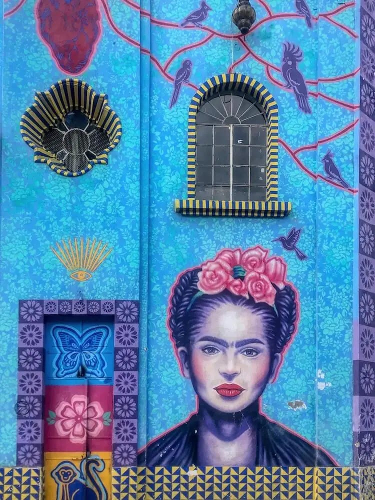 Street art - Frida Kahlo's face in pink and purple against a blue wallpaper background