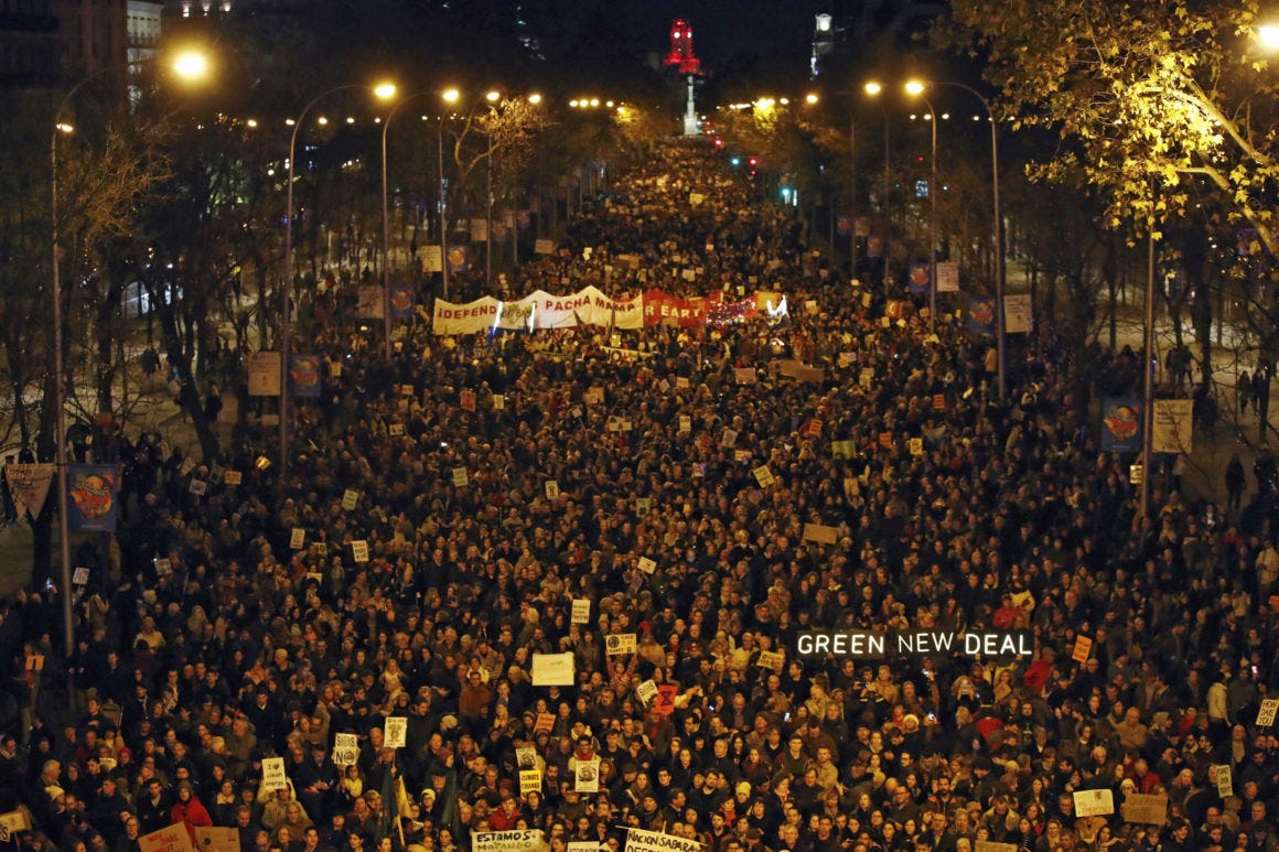 A road is blocked by a massive protest full of people holding signs reading 'Climate Justice.' It is night time. A road is blocked by a massive protest full of people holding signs reading 'Climate Justice.' It is night time.