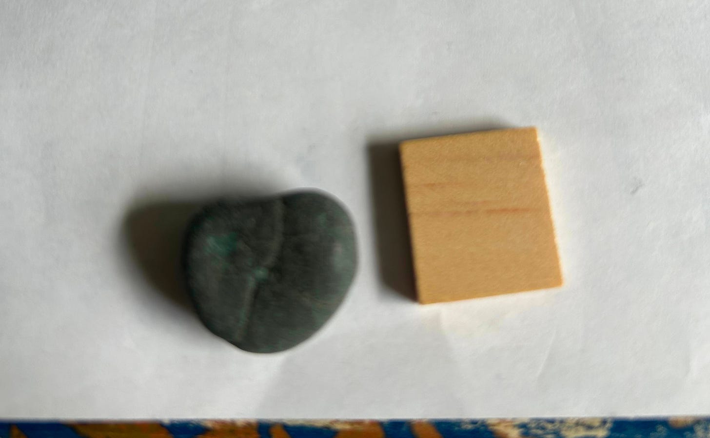 A dark gray heart shaped pebble with a crack in it next to a blank Scrabble tile on a white background.
