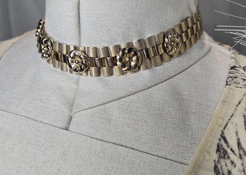 May include: A gold-toned choker necklace with a chain link design and decorative flower accents.