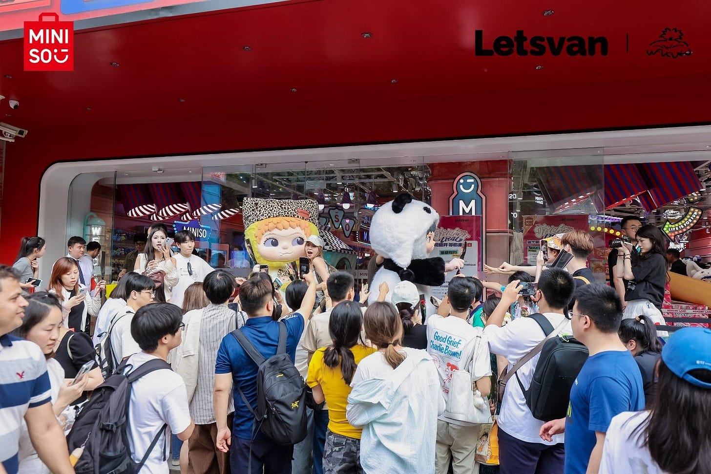 Costumed Wakuku panda and doll mascots greet excited shoppers at Miniso entrance, many filming with smartphones. Costumed Wakuku panda and doll mascots greet excited shoppers at Miniso entrance, many filming with smartphones.