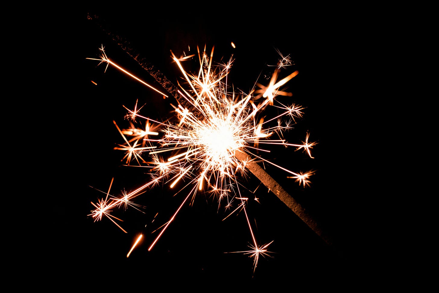 Close-up sparkler exploding with bright orange trails against a black background; star-like sparks radiate from a glowing core