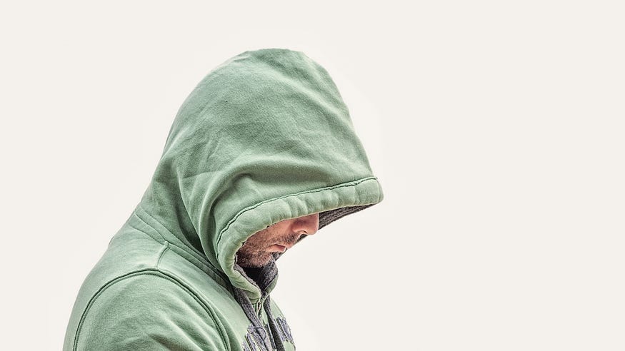 Image of a man wearing a pale green hoodie, his head bowed. Background is white. Image of a man wearing a pale green hoodie, his head bowed. Background is white.