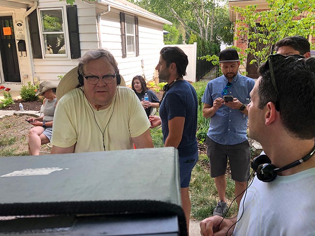 Andy Richter in a yellow t-shirt, wearing headphones looking checking a take. 