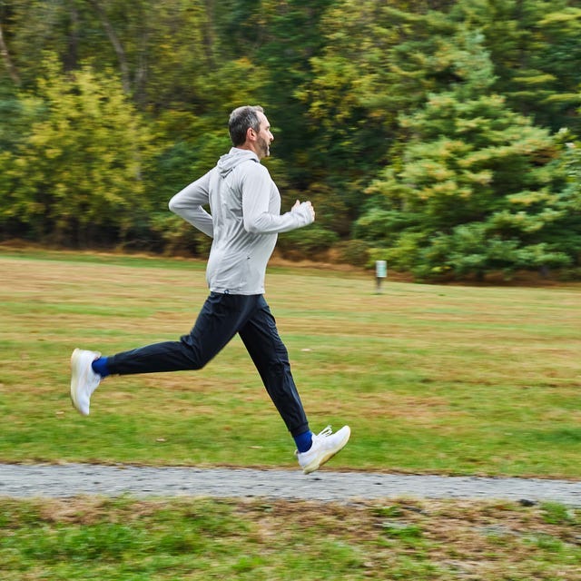A man running on a gravel path through a grassy field with trees in the background. A man running on a gravel path through a grassy field with trees in the background.